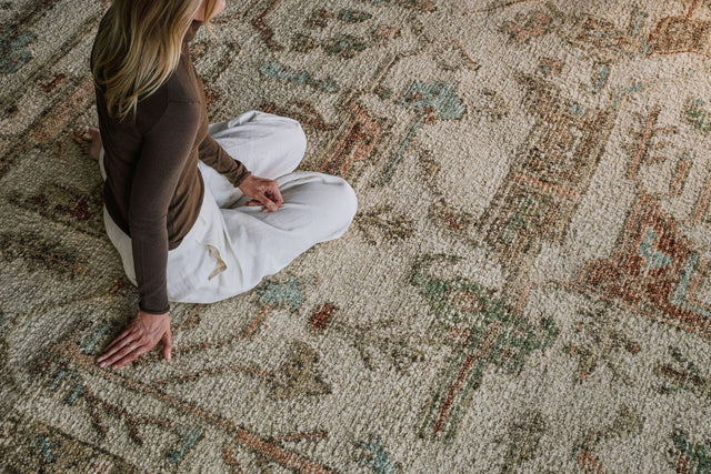Close-up of the Biraz rug from the Oushak Collection, featuring a traditional pattern in cream, olive, terracotta and turquoise beneath a tan leather chair.
