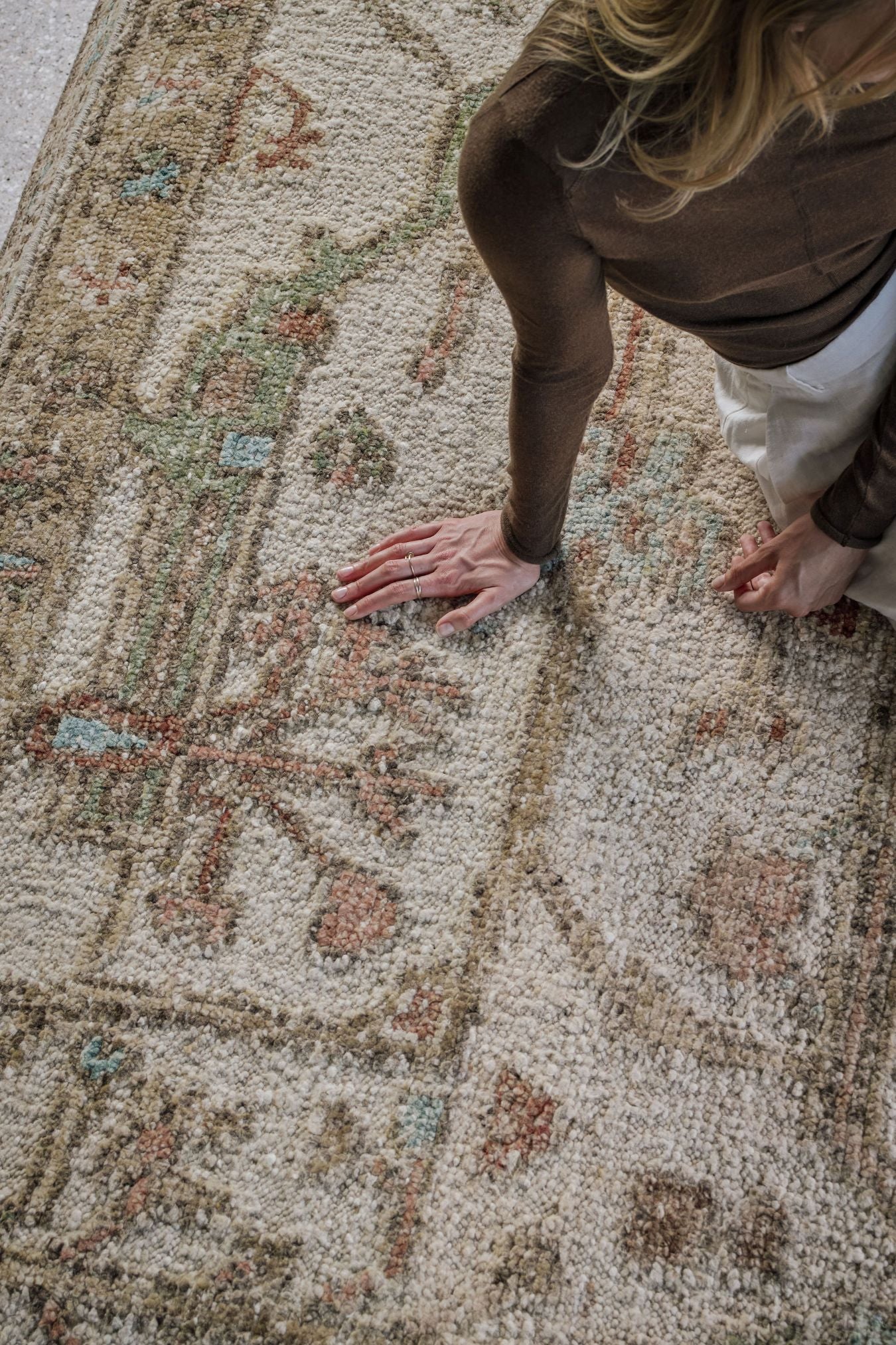 Close-up of the Biraz rug from the Oushak Collection, featuring a traditional pattern in cream, olive, terracotta and turquoise beneath a tan leather chair.