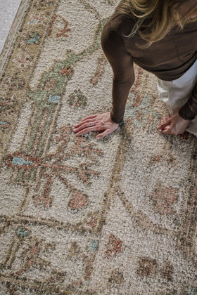 Close-up of the Biraz rug from the Oushak Collection, featuring a traditional pattern in cream, olive, terracotta and turquoise beneath a tan leather chair.