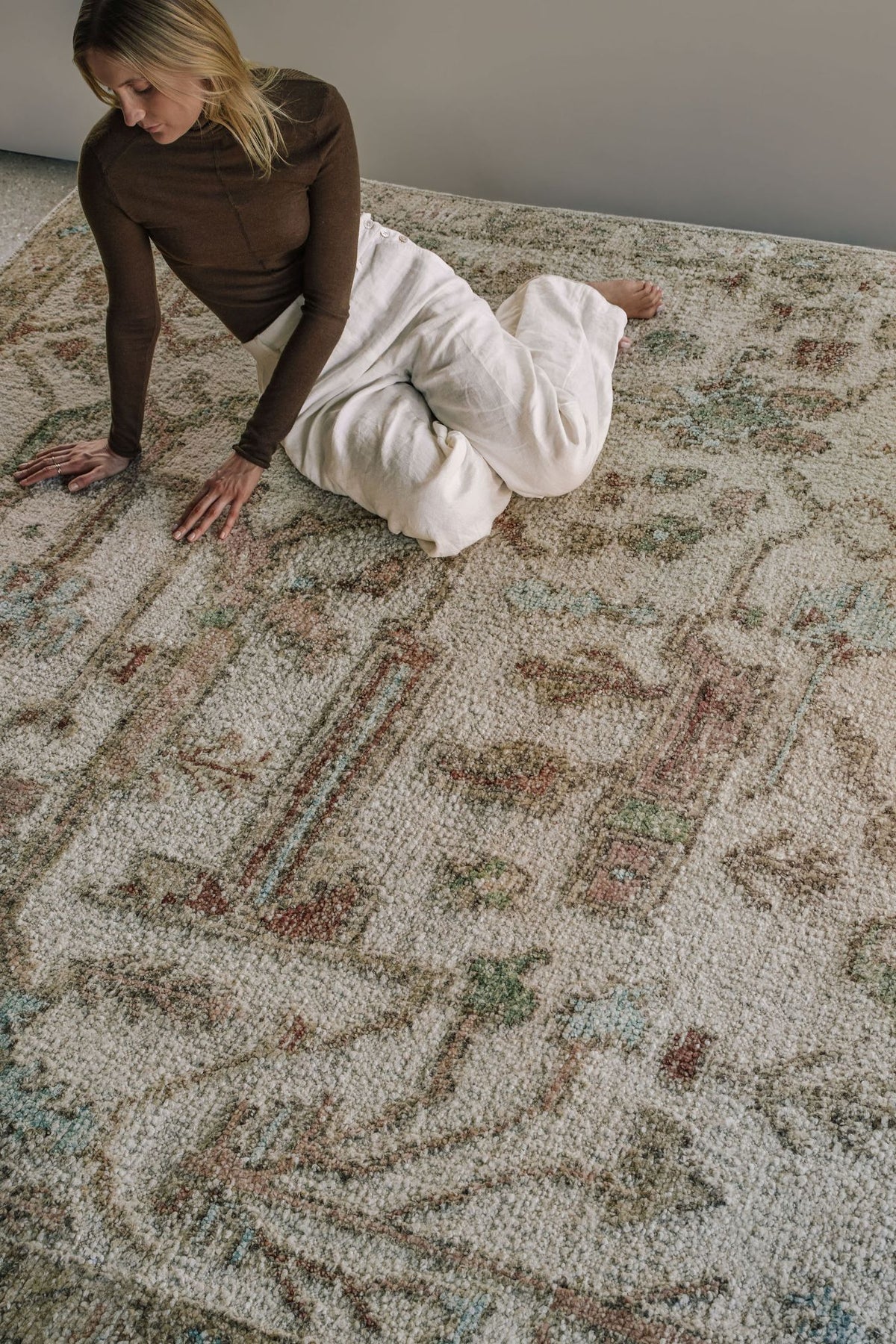 Close-up of the Biraz rug from the Oushak Collection, featuring a traditional pattern in cream, olive, terracotta and turquoise beneath a tan leather chair.