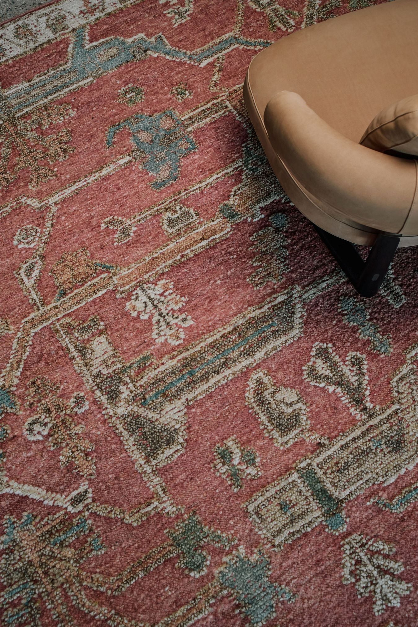Close-up of the Biri rug from the Oushak Collection, featuring a red, cream and muted blue traditional pattern beside a tan leather chair.
