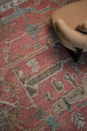 Close-up of the Biri rug from the Oushak Collection, featuring a red, cream and muted blue traditional pattern beside a tan leather chair.