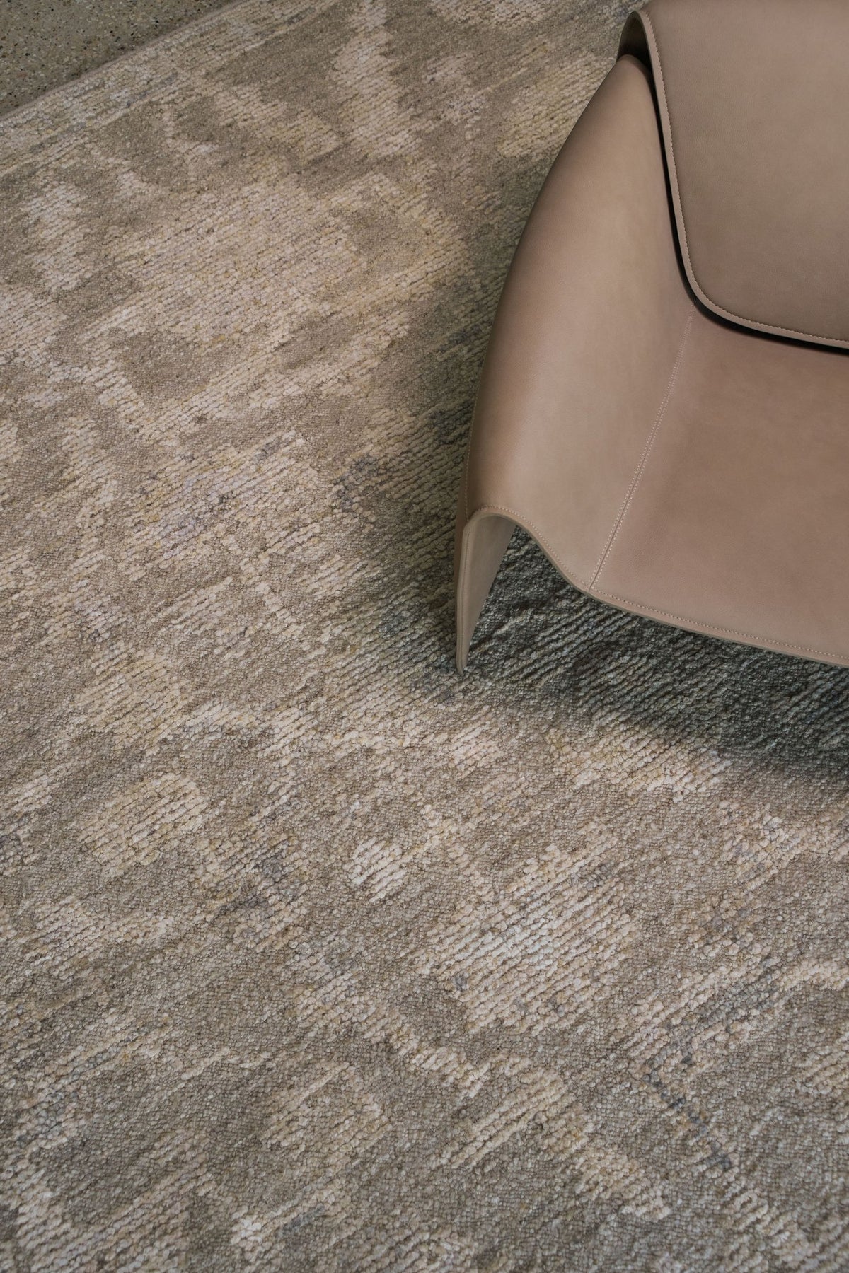 Close-up of the Olarak rug from the Oushak Collection, featuring a textured taupe, grey and cream pattern beside a soft brown leather chai