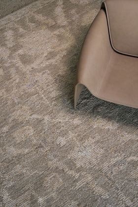 Close-up of the Olarak rug from the Oushak Collection, featuring a textured taupe, grey and cream pattern beside a soft brown leather chai