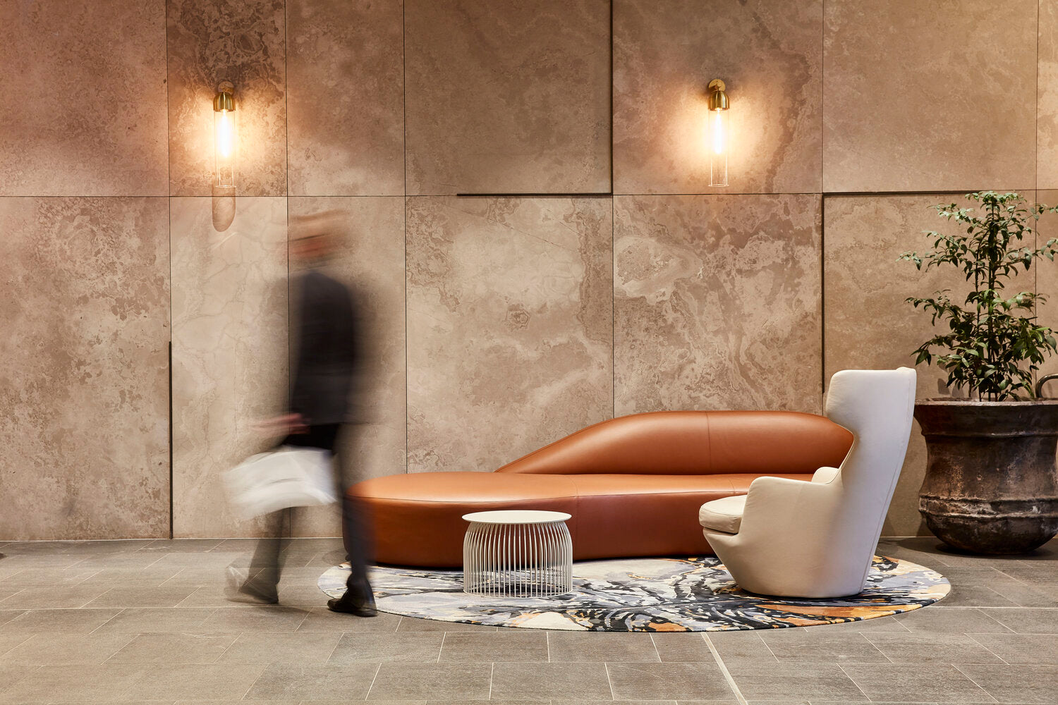 A leather sofa and armchair on a circular hand-tufted rug in a stone-clad lobby