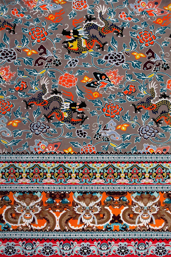 A close-up of a patterned textile or rug showing a gray-brown ground with repeated stylized dragon motifs, floral elements, and a decorative border with orange, red, blue, black, and white details.
