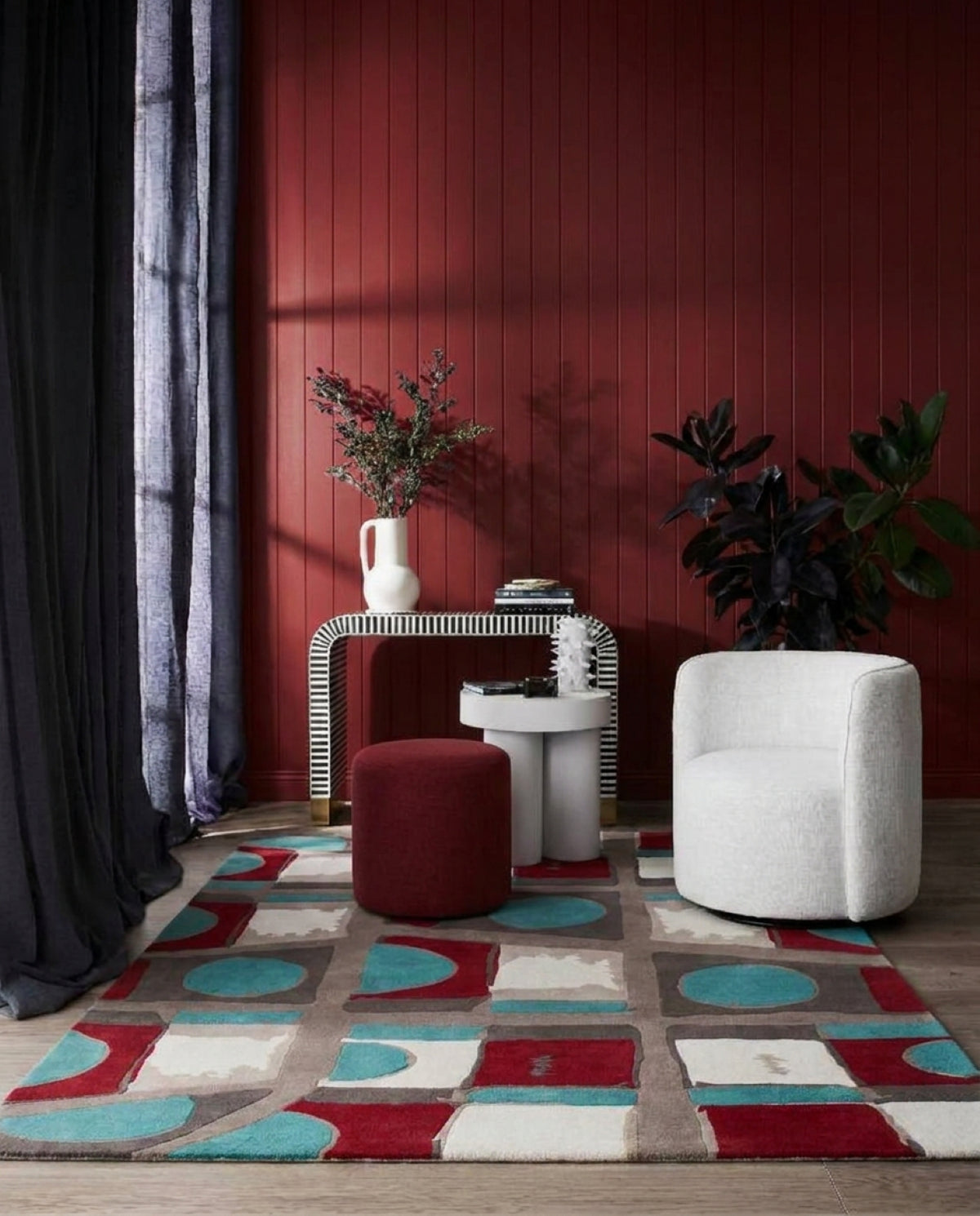 A modern living room scene featuring a colorful geometric area rug with red, teal, beige, and white blocks. The Boulevard rug was designed by designer Rugs