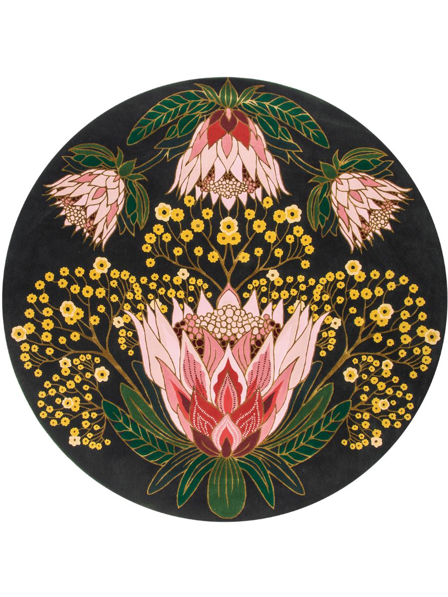A circular black rug featuring a detailed botanical pattern with pink protea-like flowers, green leaves, and clusters of small yellow flowers, shown on a plain white background.