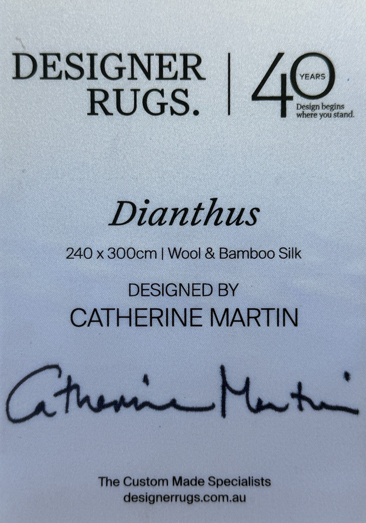 A close-up of a rug label or product card for Designer Rugs, featuring the design name 'Dianthus', dimensions '240 x 300cm', material 'Wool & Bamboo Silk', designer 'Catherine Martin', and a signature. The card is light blue with black text.