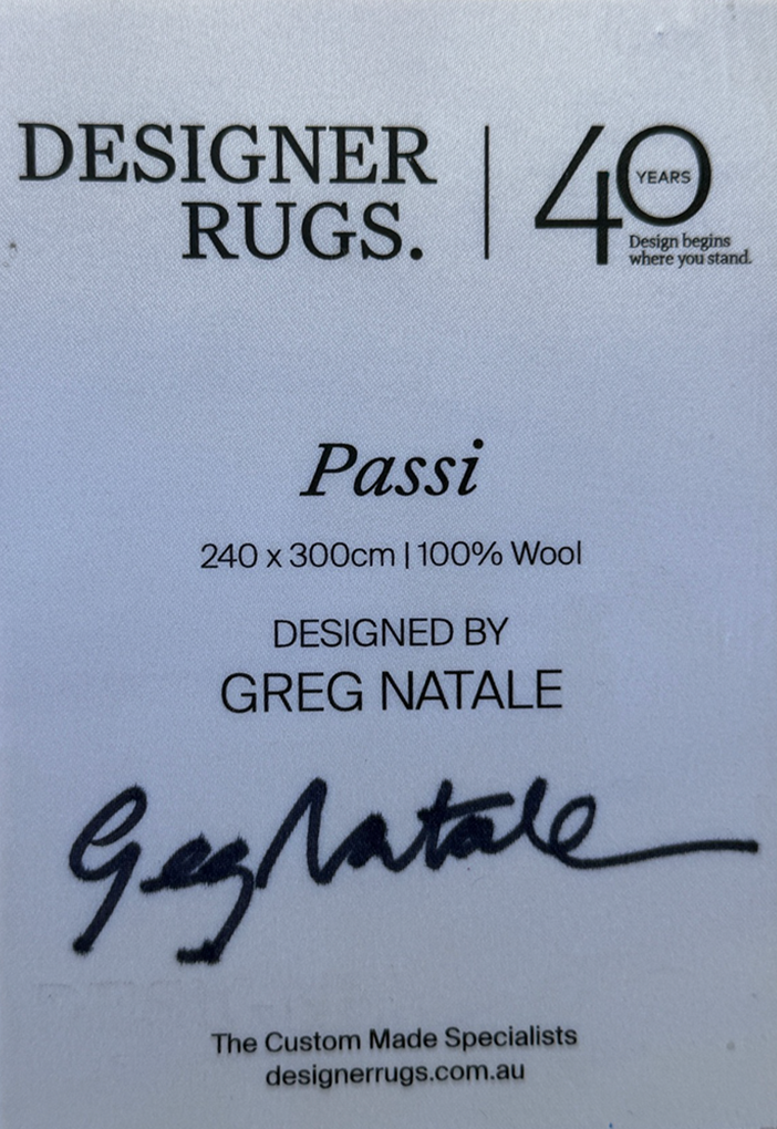 A white product information card for Designer Rugs Passi, featuring black text with dimensions 240 x 300cm, 100% wool, designed by Greg Natale, and a signature.