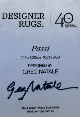 A white product information card for Designer Rugs Passi, featuring black text with dimensions 240 x 300cm, 100% wool, designed by Greg Natale, and a signature.