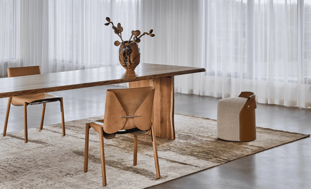 A timber dining table and chairs on a pale rug beside a window