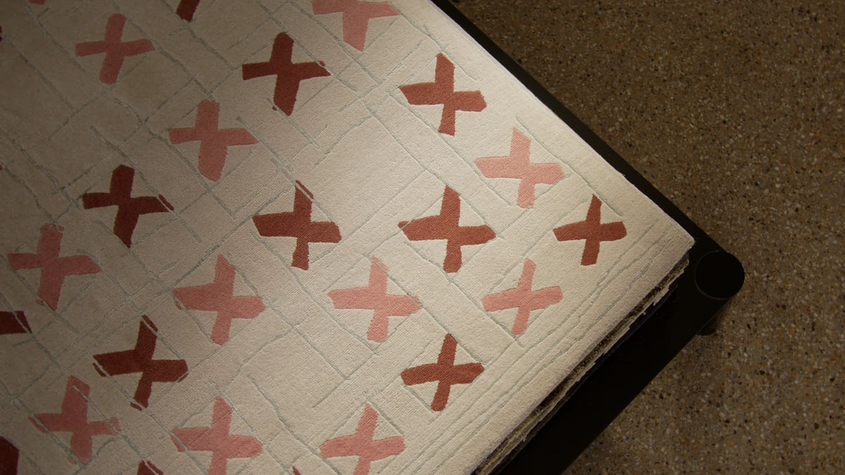 A cream hand-tufted rug with terracotta cross motifs, rolled at the edge